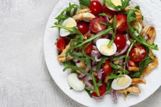 A warm salad with fried chicken fillet, arugula and cherry tomatoes, and boiled quail eggs, on a