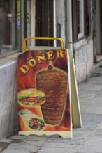 Poster stand with doner kebab in front of a snack, Venice, Veneto, Italy