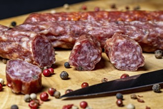 Close-up of salami slices with peppercorns and a knife on wood, crunchy pepperbeiser sausage