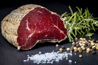 Delicious sausage with salt and pepper on a dark slate plate, delicacy ham fresh from the butcher