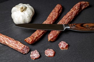Sliced salami next to a knife, accompanied by garlic, crunchy Pfefferbeiser sausage