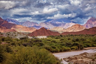 River flows through green vegetation against a mountain backdrop with red hills, the landscape and