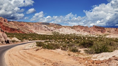 Road snakes through red rocky landscape under a cloudy sky, the landscape and colorful rock
