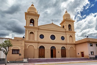 Front view of a church with two bell towers, in front of an empty forecourt under partly cloudy