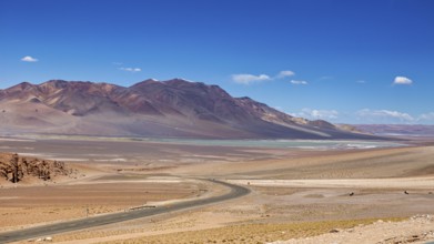 A long road snakes through an arid desert landscape with distant mountains, the countryside and