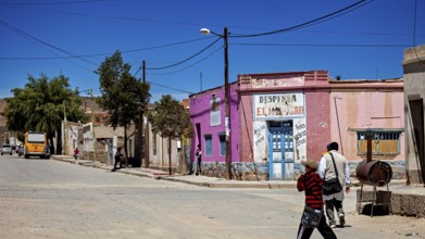 Colourful buildings and people in a bright, dry village with hills in the background, San Antonio