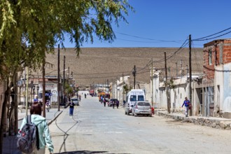 Busy street in a small village surrounded by dusty hills under bright sunshine, San Antonio de los