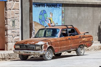 A rusty car stands on a dusty road in front of a colorful mural, Old car in traffic in San Antonio