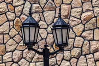Two vintage style black lanterns in front of a stone wall, two old street lamps in front of a