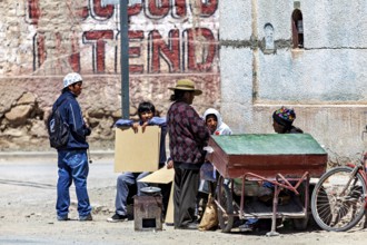 A group of people stand and sit in front of a wall in a street scene, people in the streets of San