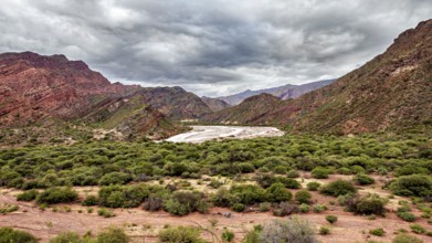 A green valley surrounded by mountains under a cloudy sky, the landscape and colorful rock