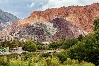 Colourful mountains rise from a green, overgrown desert under cloudy skies, the landscape and