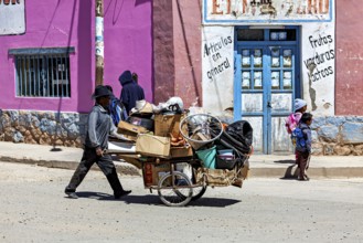 Man pulls a cart full of boxes along a colorful street, people in the streets of San Antonio de los
