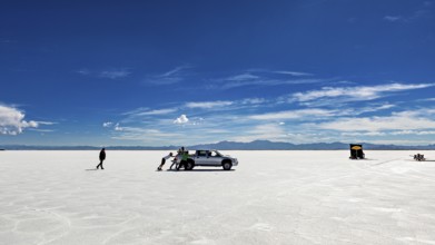 People push a car on a wide salt lake under a blue sky, The Salar de Cauchari salt pan near Salta