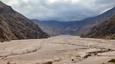 Wide valley between two dark mountain ranges under a cloudy sky, the landscape and colorful rock