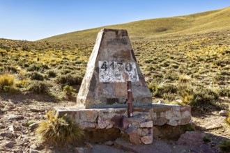 Stone pyramid with altitude marker at 4130 meters, surrounded by dry desert landscape under blue