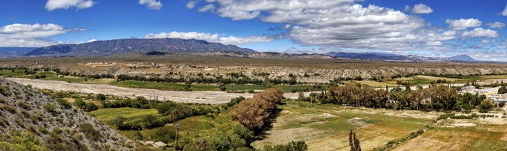 Panoramic view of green valleys and distant mountains under a cloudy sky, roads through the