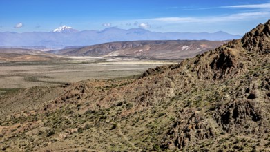 Vast desert with rocky mountain range and blue sky in the background, roads through the Quebrada de