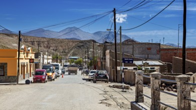Several cars in a hilly desert town surrounded by mountains under blue skies, San Antonio de los