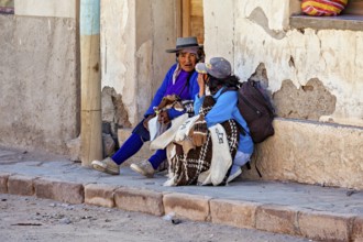 Two woman in traditional clothes talking on a wall, people in the streets of San Antonio de los