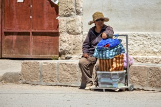Man wearing hat sitting on the side of a road next to a loaded cart, people in the streets of San
