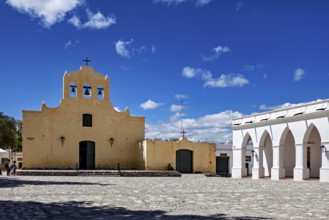 Yellow church with bell tower in front of a large square under bright blue sky, Iglesia San José de
