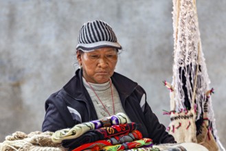 A woman in traditional clothing looks at handmade textiles with serious expression, tourist and