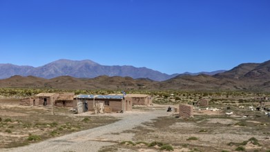 Cabins in an open desert landscape with dry soil and mountains in the background, San Antonio de