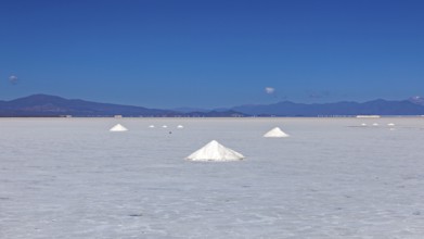 Wide salt desert with salt formations in the foreground and mountains on the horizon under clear