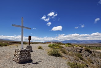 A cross stands on a hill with wide views of mountains and wide skies, roads through the countryside