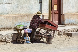 Man working on a red-roofed cart on the street corner, people in the streets of San Antonio de los