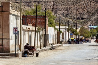 People walk along a picturesque rural road with old buildings and trees, San Antonio de los Cobres,