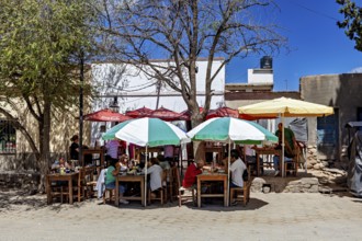 Outdoor area with dining tables and colorful umbrellas where people sit in the shade in sunny