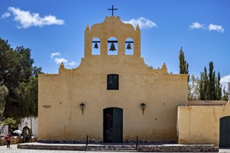 Front view of a yellow church with bells and cross under a blue sky, Iglesia San José de Cachi in
