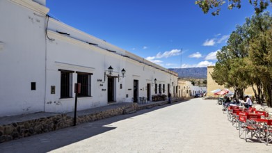 Wide street with white buildings and a patio with red chairs under a clear blue sky, Downtown Cachi