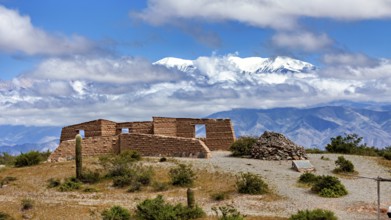 Old stone ruin in a desert-like landscape with mountains in the background and snow-capped peaks,