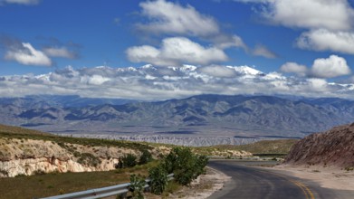 Curvy road leads through a vast landscape with mountains and clouds in the sky, roads through the