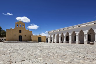 Square with yellow church and white arcades under bright blue sky, Iglesia San José de Cachi in