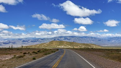 An empty, winding road leads through a vast desert landscape under a cloudy sky, The landscape of