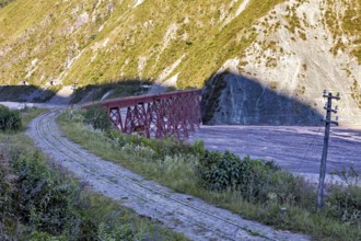 Abandoned railway line with red bridge in a mountainous landscape with lots of vegetation, roads