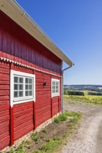 Red wooden rural barn beside a gravel road with a scenic landscape view in the countryside a sunny