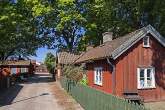 Peaceful Scandinavian street lined with traditional red wooden houses with green picket fence and
