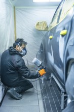 Auto body technician wearing mask and gloves sprays primer onto a car door panel inside a