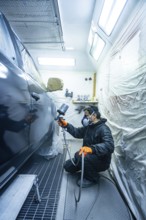 Automotive technician wearing protective mask and gloves, using a spray gun to apply fresh paint to
