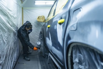 Auto body technician working in a repair shop, carefully applying paint primer to a vehicle door