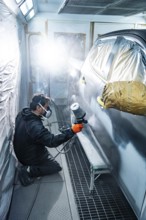 Professional auto body mechanic kneeling while applying primer or paint to a passenger cars side