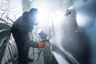 Auto mechanic applying primer paint to a car body panel using a spray gun in a well lit automotive