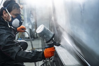 Professional auto body painter wearing a respirator mask and protective gloves expertly applying