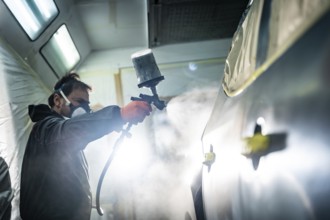 Auto body technician wearing protective mask and gloves applying a fresh coat of paint primer to a
