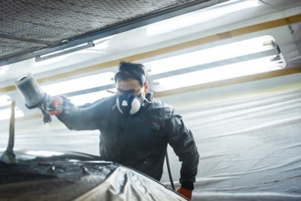 Auto body technician working in a specialized workshop, wearing a respirator mask and protective
